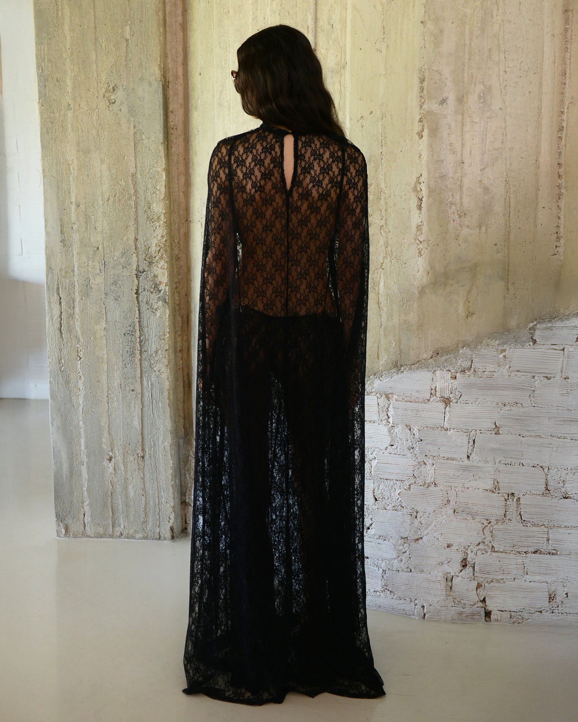 Person wearing a black lace outfit standing in a room with textured walls.