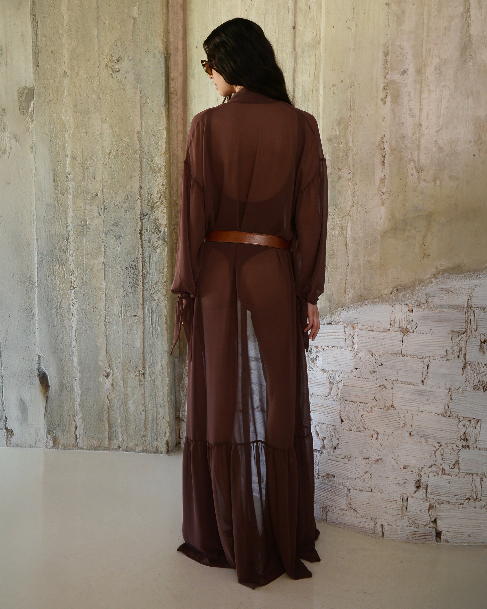 Person wearing a brown outfit standing against a textured wall.