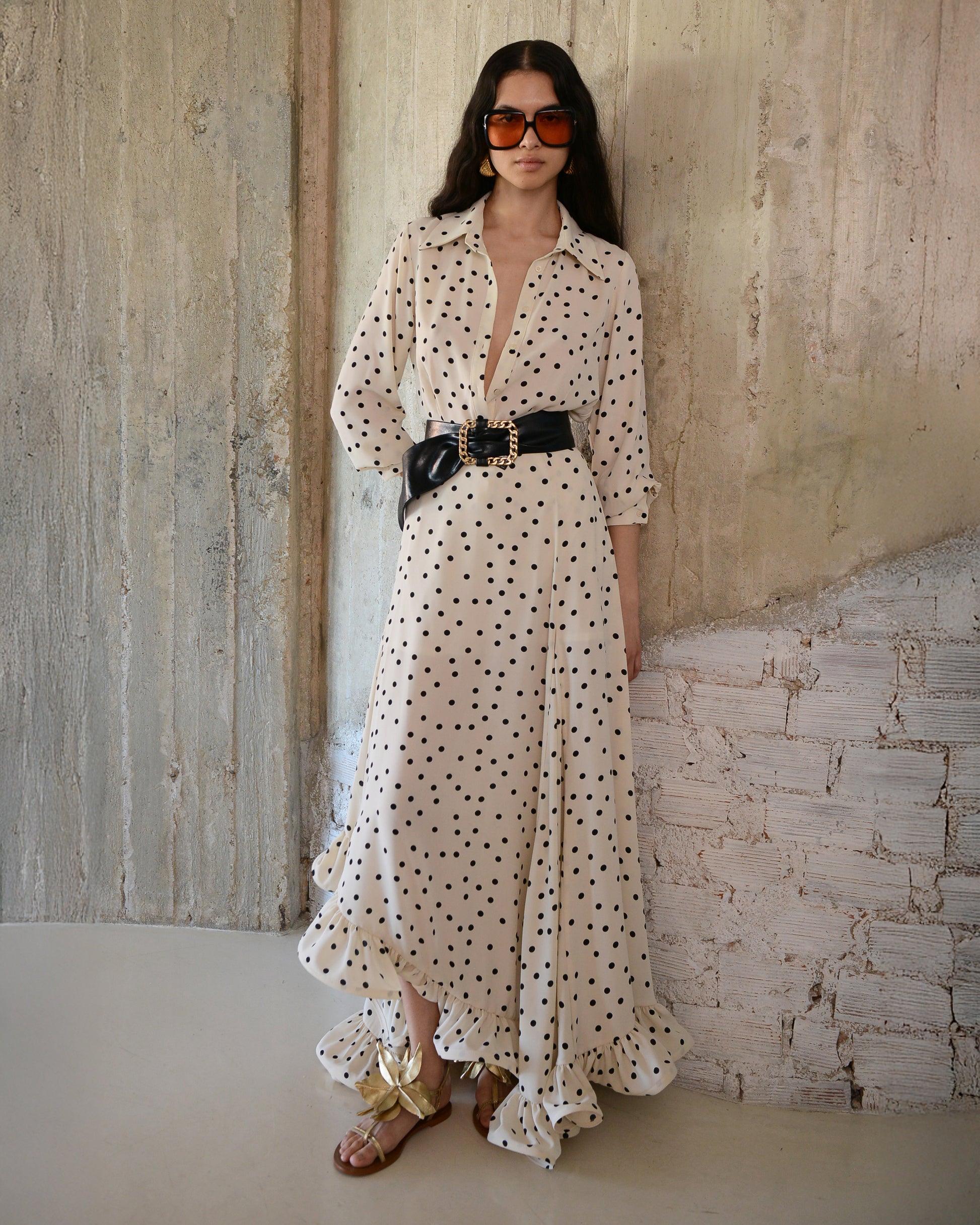 Woman in a polka dot dress standing against a textured wall.