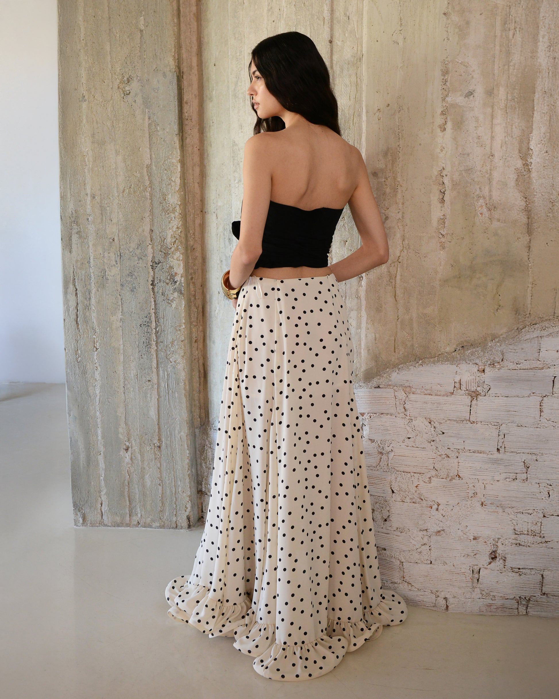 Woman wearing a black top and white polka dot skirt against a textured wall.