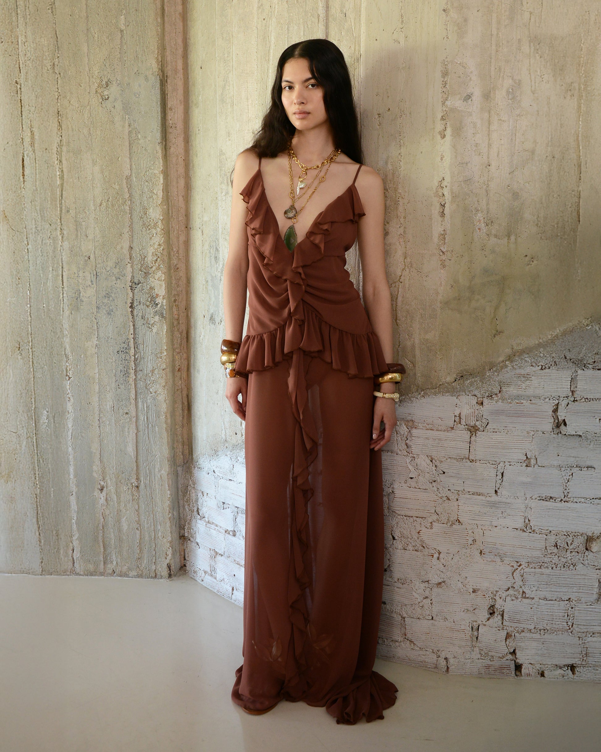 Woman wearing a brown dress standing against a textured wall.