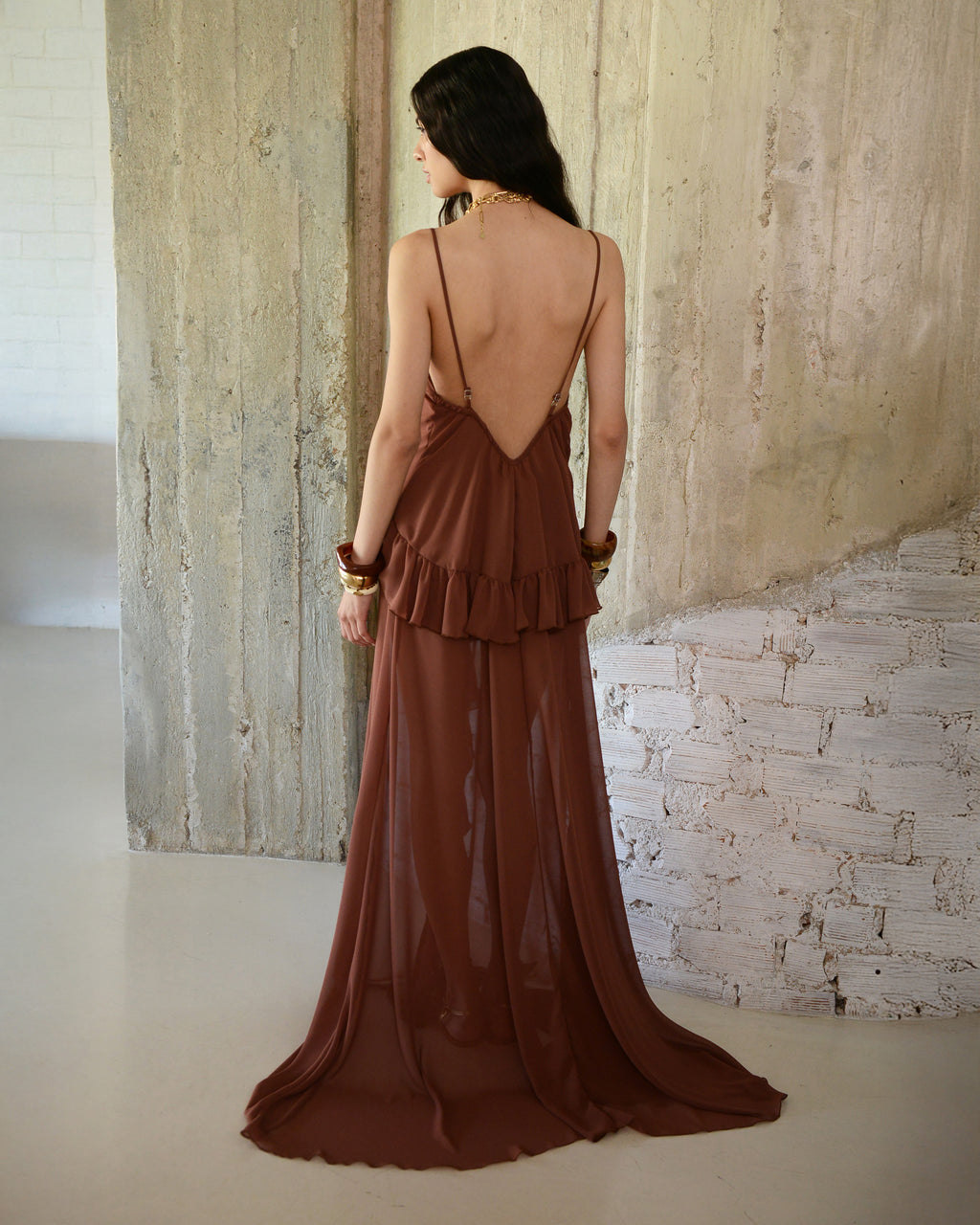 Woman wearing a brown dress with a backless design, standing against a textured wall.