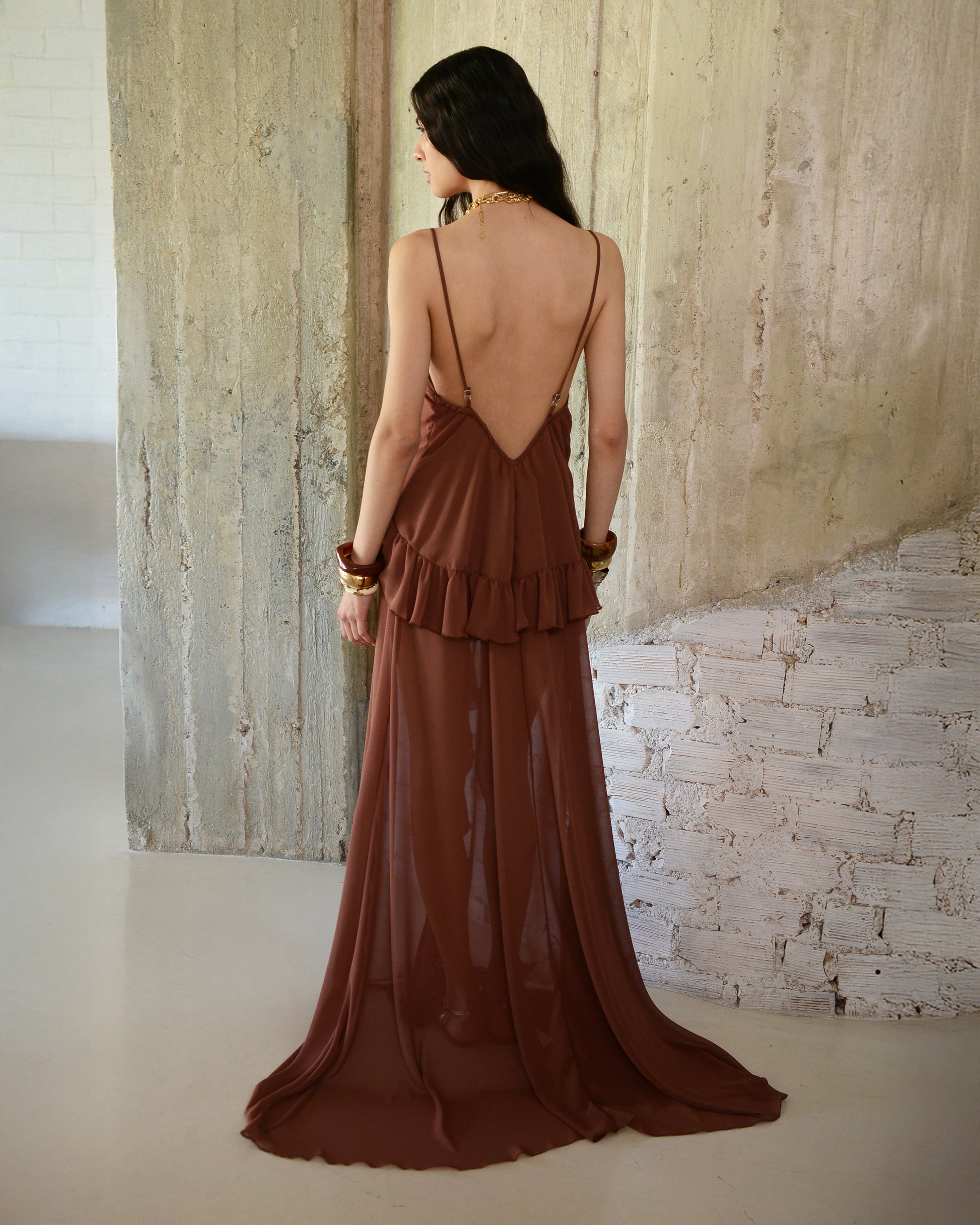 Woman wearing a brown dress with a backless design, standing against a textured wall.