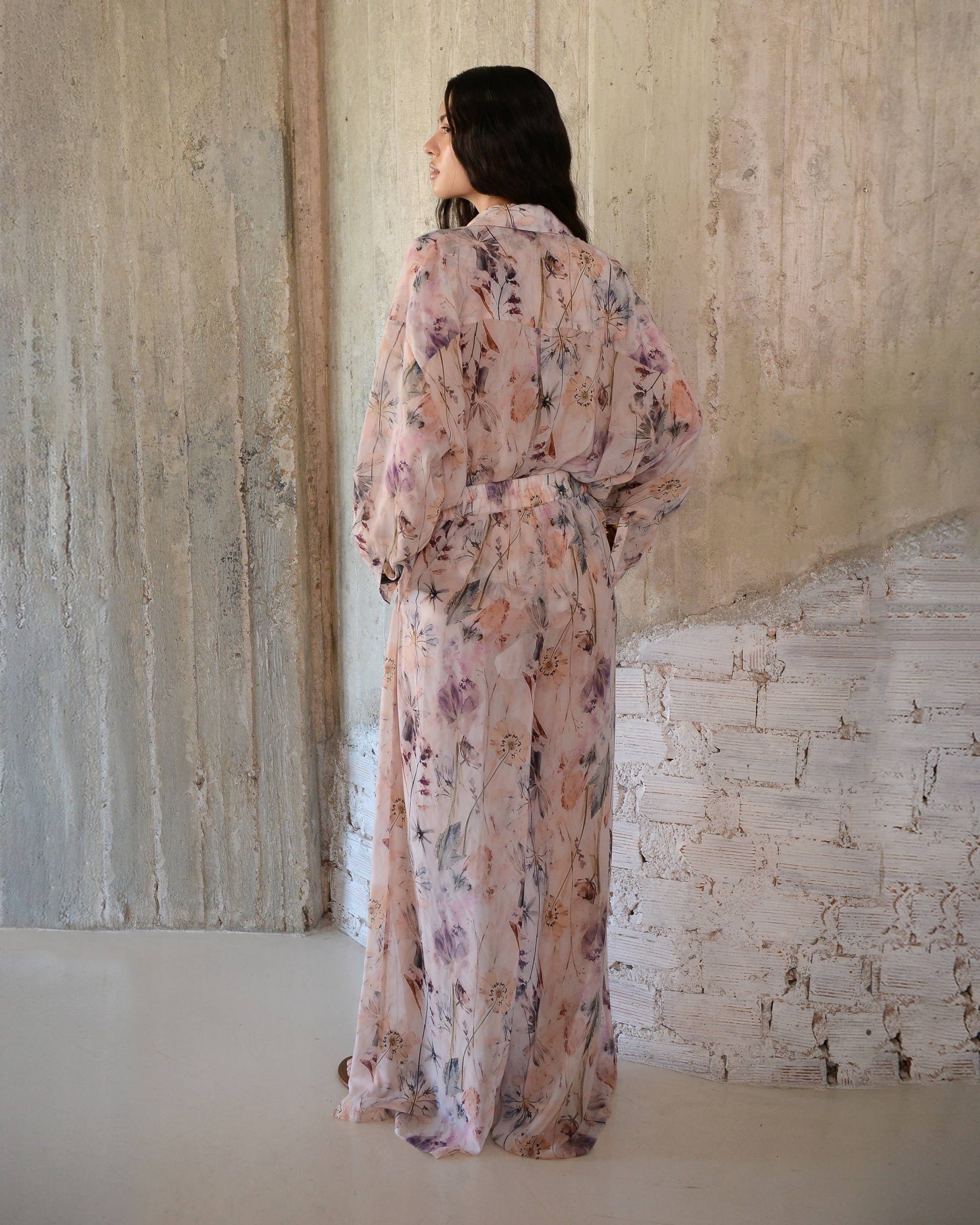 Woman wearing a floral dress standing against a textured wall.