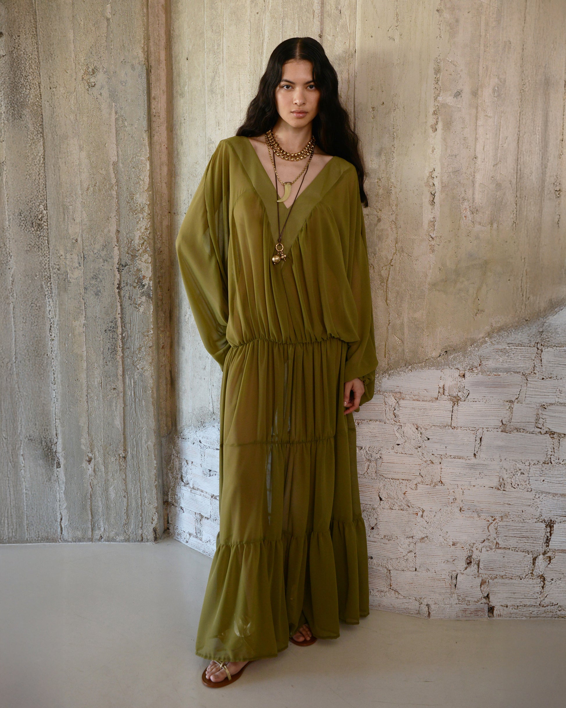 Woman wearing a green dress standing against a textured wall.