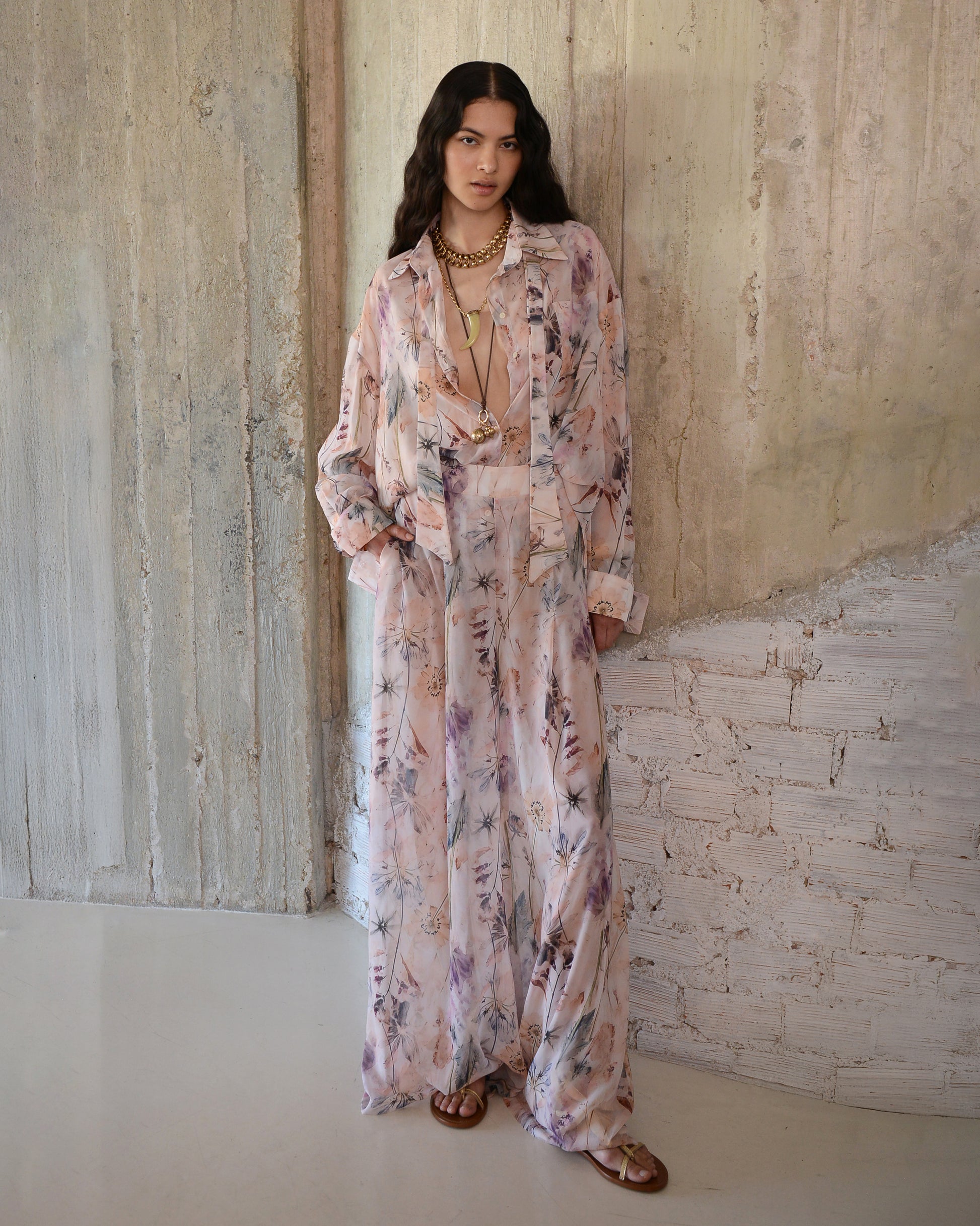 Woman wearing a long floral dress standing against a textured wall.