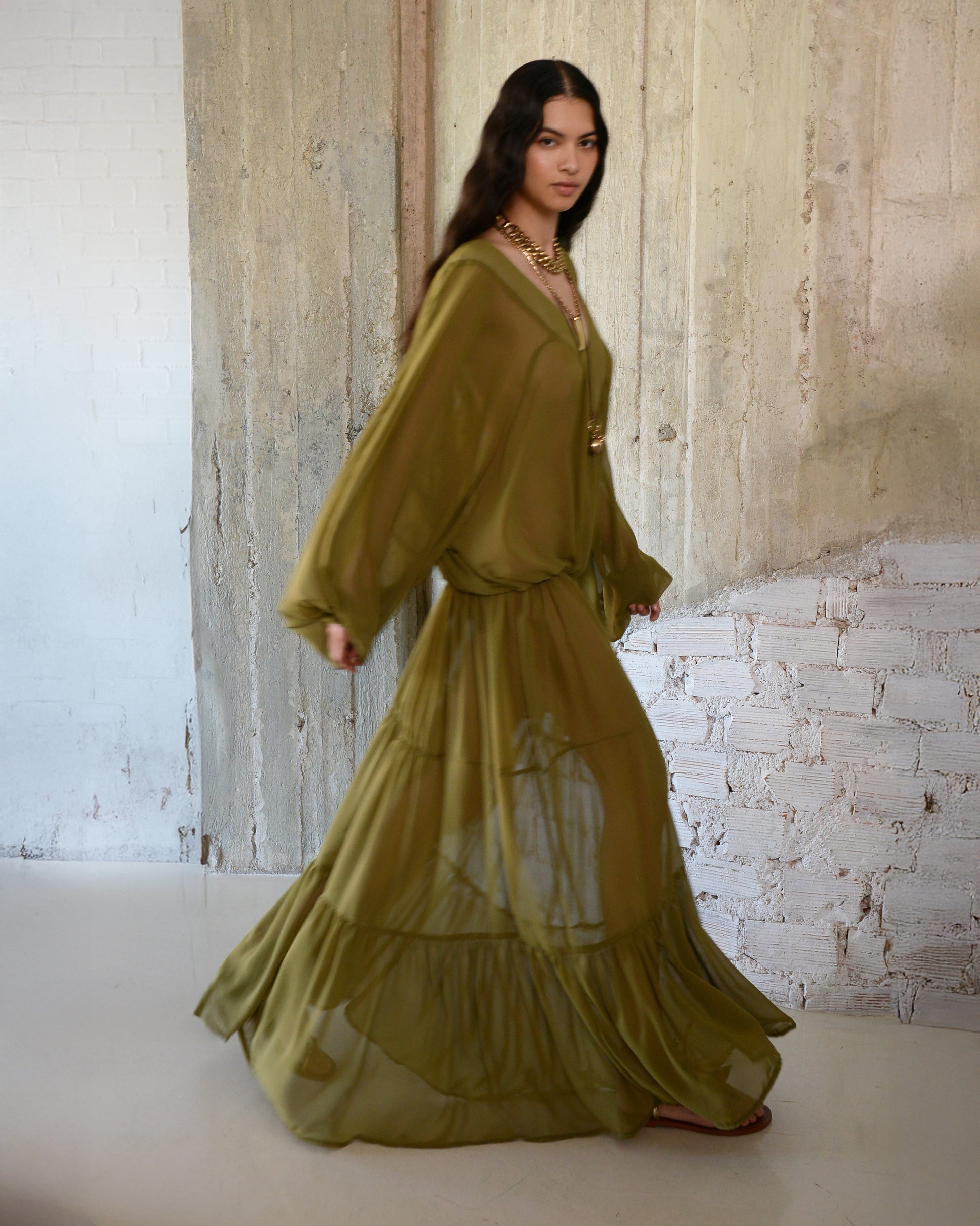Woman wearing a long, flowing green dress against a textured wall.
