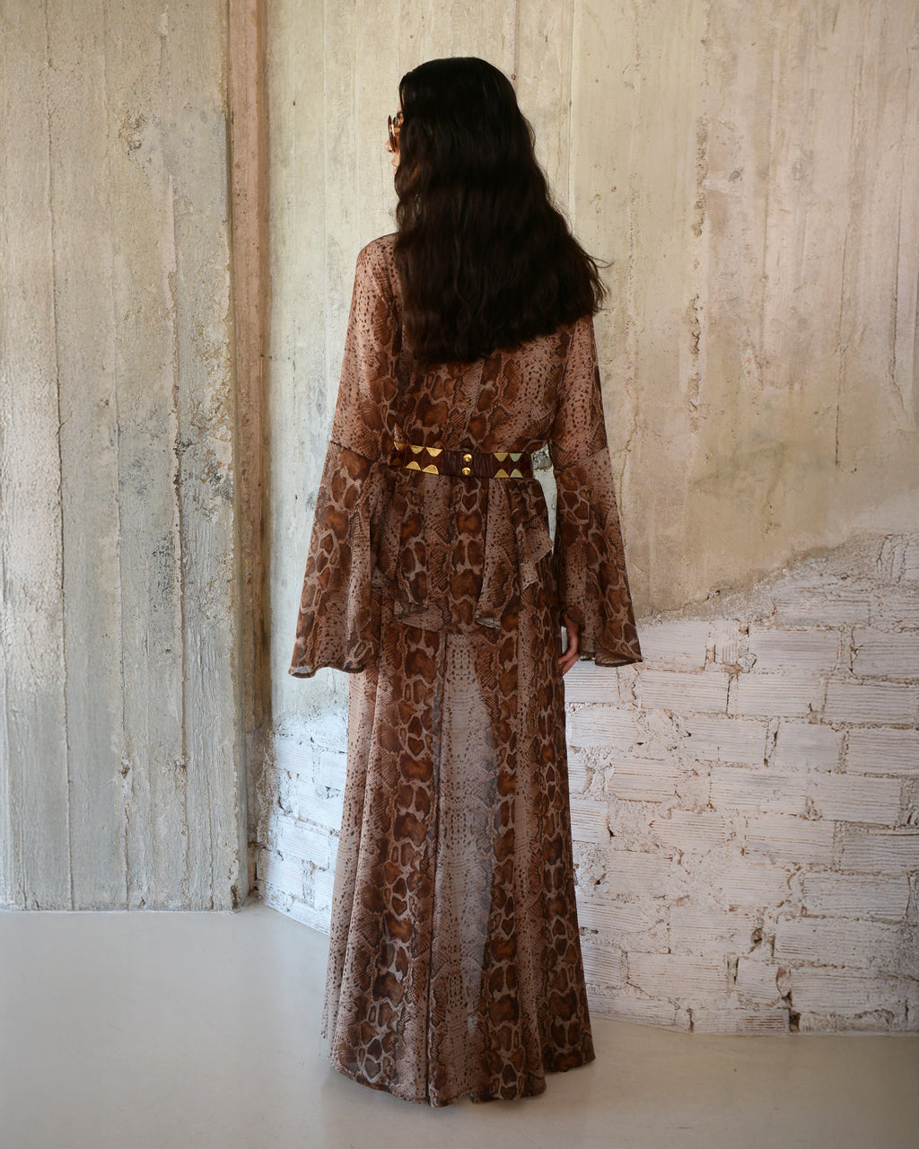 Woman wearing a long, patterned dress standing against a textured wall.