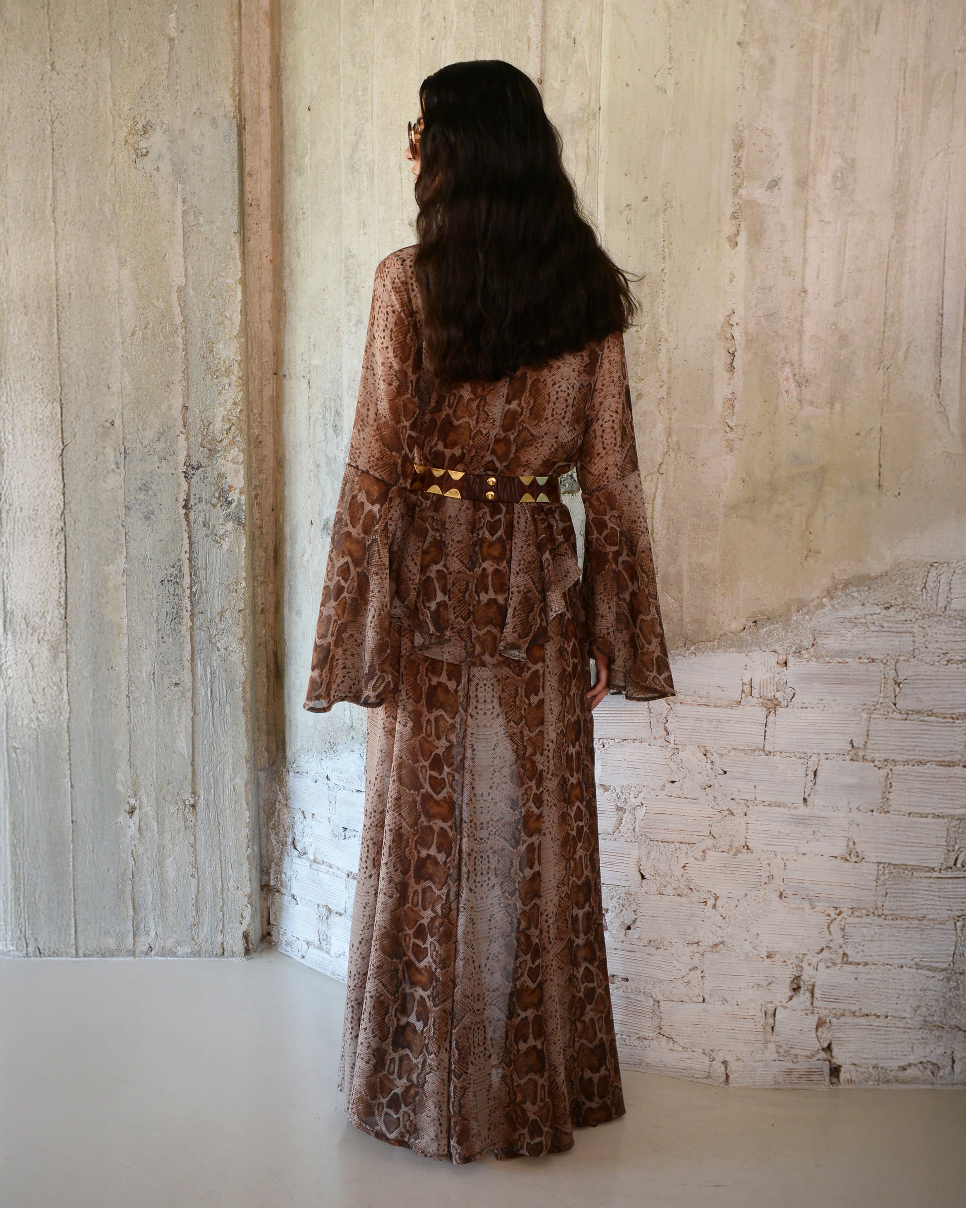 Woman wearing a long, patterned dress standing against a textured wall.