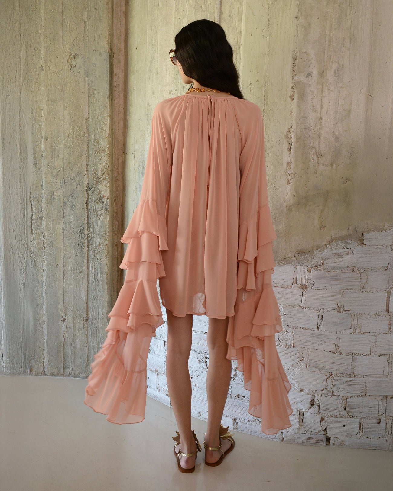 Woman wearing a peach-colored layered dress against a textured wall.
