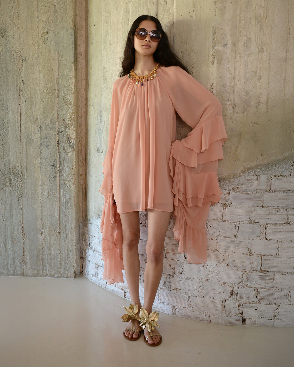 Woman wearing a peach dress with ruffled layers against a textured wall.