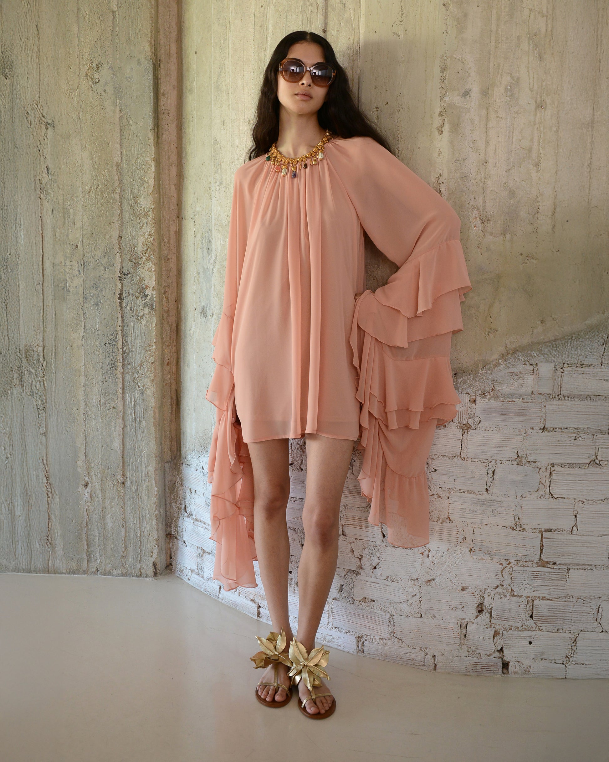 Woman wearing a peach dress with ruffled layers against a textured wall.